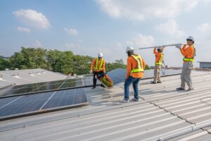 Men technicians carrying photovoltaic solar moduls on roof of factory on the morning. Installing a Solar Cell on a Roof. Solar panels on roof. Workers installing solar cell power plant eco technology.