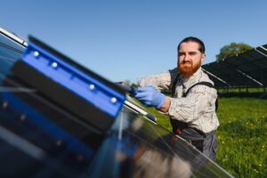 Male worker cleaning solar panels with a special tool, ensuring efficiency in a solar energy farm, contributing to renewable energy