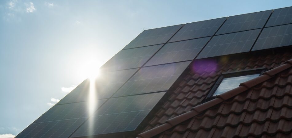 Solar panels installed on a sloped red-tiled roof with sunlight shining behind them, potentially qualifying for the Federal Solar Tax Credit 2026.