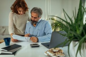 A man and woman review paperwork together at a table with a laptop, calculator, notebooks, coffee mug, and potted plant while discussing the Federal Solar Tax Credit 2026.